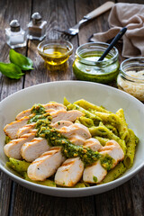 Penne with basil pesto sauce and grilled chicken breast on wooden table