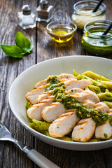 Penne with basil pesto sauce and grilled chicken breast on wooden table
