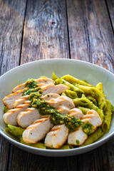 Penne with basil pesto sauce and grilled chicken breast on wooden table