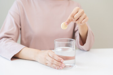 Close up young woman hand putting or dropping effervescent tablet into glass of water, holding pain pill, painkiller medicine, aspirin for treatment, take vitamin c for hangover. Health care concept.