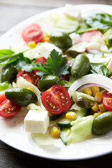 Salad with Feta Cheese, Green Olives, Baby Spinach, Cucumber, Cherry Tomatoes and Capers. Dark wooden background. Close up.	