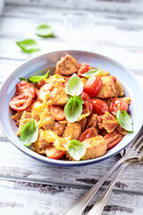 Farfalle pasta with chicken breast, cherry tomatoes and fresh basil. Bright wooden background. Close up.