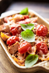 Baked farfalle pasta with chicken breast, cherry tomatoes and mozzarella cheese. Rustic wooden background. 