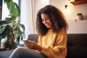 Happy young latin woman sitting on sofa holding mobile phone using cellphone technology doing ecommerce shopping, buying online, texting messages relaxing on couch in cozy living room, Generative AI