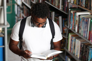 male African university student in white t-shirt with backpack reads an interesting book in the...