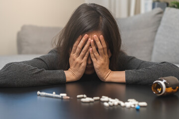 Anti, drug addict asian young woman hand cover face in front of pills, medicament with narcotic syringe on table, abuse overdose. Sick pain of health, unhealthy people. Suicide depressed or despair. - obrazy, fototapety, plakaty
