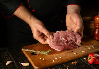 The cook is preparing a barbecue of veal steak on the kitchen table. Chef's hands with a cut piece...