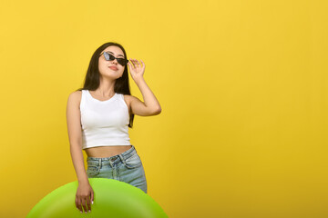 Modern teenage girl in fashionable clothes enjoying the sun, posing on a yellow background....