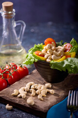 Dried cashew nuts, along with fresh vegetables, are beautifully laid out on a dark textured table and dishes. Beautiful serving of healthy vegetables and nuts for a hearty vitamin breakfast.
