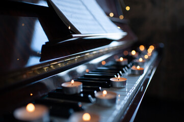 Burning candles stay on vintage piano keys over glow lights at background. Romantic atmosphere.