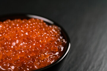Red Caviar in a black bowl over black background.