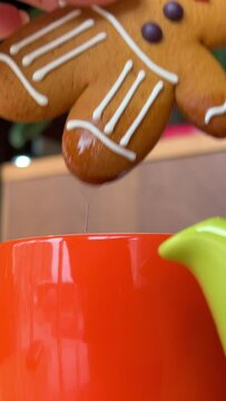 Festive Christmas food with gingerbread men, Close up shot of a hand dipping a biscuit into a cup of coffee fruit cake and shortbread cookies, and reindeer ornaments centrepiece with blinking