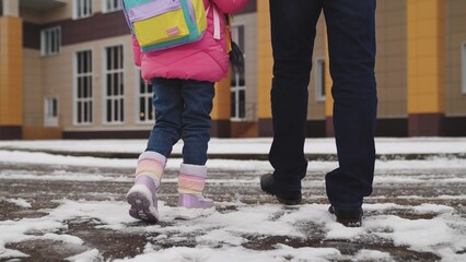 legs close-up, walking snow, child his father walk with their feet snow school building, child school backpack holds his father hand, little student goes class, parental support hand, cold snowy road - obrazy, fototapety, plakaty