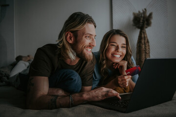 Happy loving couple looking at laptop and using credit card while shopping online from home