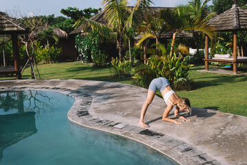 Slim woman doing wide stance forward bend yoga on poolside