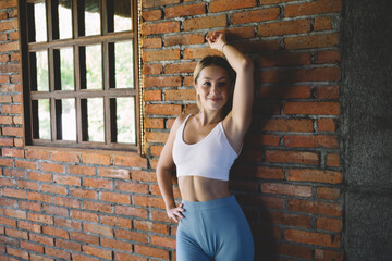 Smiling slim woman standing near window of brick wall