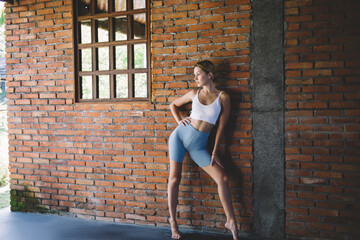 Slim woman standing like model near brick wall