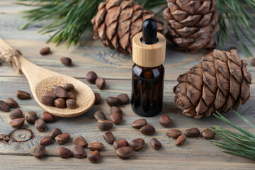 Cedar essential oil amber glass bottle, whole unshelled nuts on bamboo spoon, pine cones and green needle branches on wooden table.