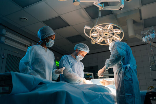 Low-angle view of diverse cooperating team of doctors, surgeons and African-American nurse processing surgical operation in operating room modern hospital emergency department. Concept of surgery.