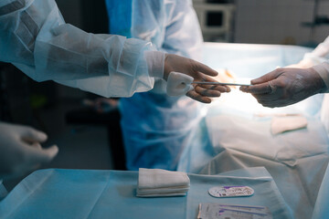 Cropped side view of unrecognizable nurse assists surgeons, giving surgical clamp with tampon...