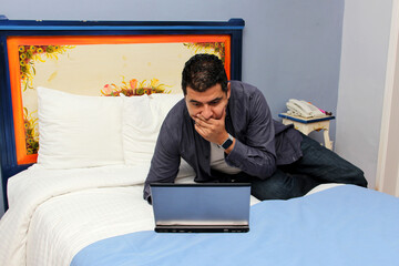 40-year-old dark-skinned Latin man works on his laptop on the bed, does home office and overworks, which causes stress