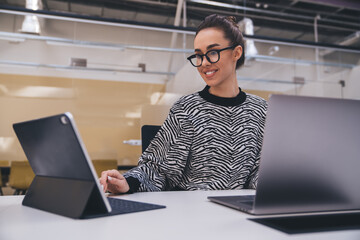 Cheerful young female freelancer working on laptop indoors