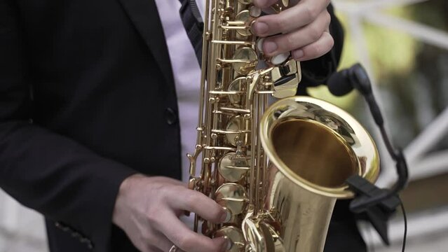 A saxophonist in a suit playing a golden saxophone outdoors with a blurred greenery background, a classic image of live jazz music.