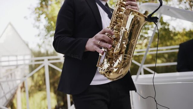 A saxophonist in a suit playing a golden saxophone outdoors with a blurred greenery background, a classic image of live jazz music.