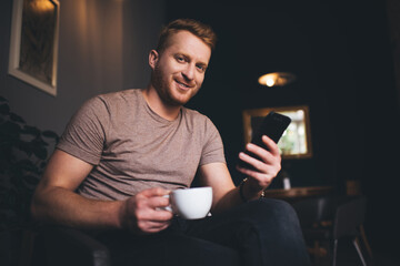 Portrait of happy Caucasian man with coffee cup and modern smartphone technology smiling at camera...