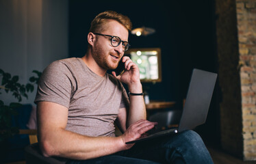 Positive man speaking on cellphone while working remotely on computer