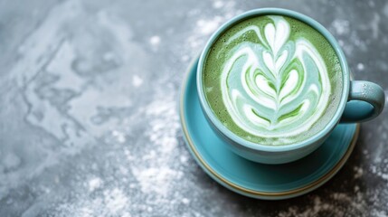 A soothing cup of matcha latte with a heart-shaped design in the froth is served in a speckled ceramic cup, with matcha powder sprinkled on the saucer and table.