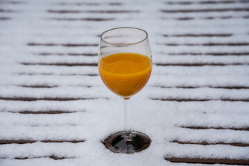 Glass of organic fresh squeezed orange juice on snow covered table at garden. Healthy eating lifestyle background. Energy shot before winter sport activities - skiing, etc. Natural Vitamin C booster.