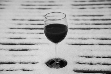 Glass of red wine on a snow covered table in the garden in winter. Sad happy hour. Memories. Black white historic photo.