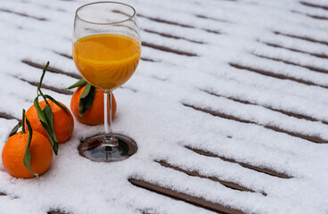 Glass of organic fresh squeezed mandarin juice on a snow covered table in garden and tangerine fruits. Healthy eating lifestyle background. Energy shot before winter sport activities - skiing, etc.