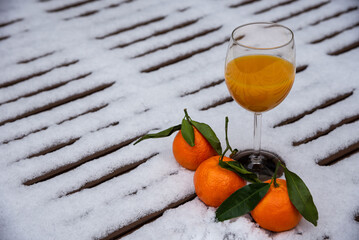 Glass of organic fresh squeezed mandarin juice on a snow covered table in garden and tangerine fruits. Healthy eating lifestyle background. Energy shot before winter sport activities - skiing, etc.