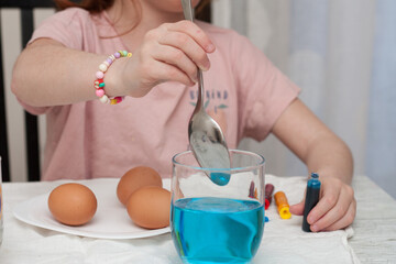 little girl dyeing easter eggs at the living room table. Horizontal. Faceless.