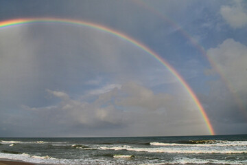 Cloudy sky with a double rainbow over the ocean at the beach