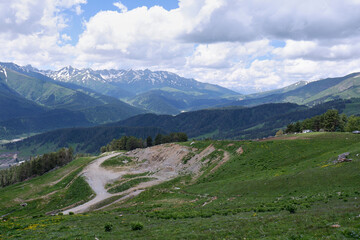 View of idyllic mountain scenery with fresh green meadows blooming on a beautiful sunny day, snow-capped mountains in the distance