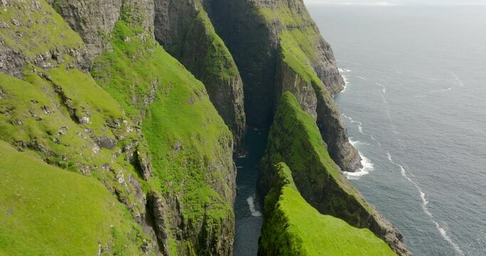 Aerial Seagulls Flying Around Green Rock Formations In Wavy Sea, Drone Flying Forward On Sunny Day - Faroe Islands, Denmark
