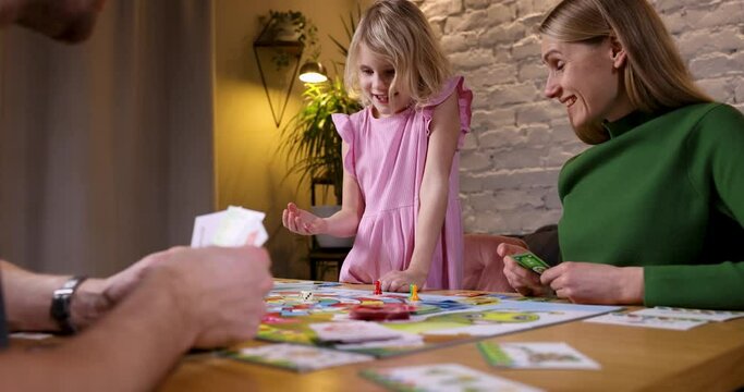 family having fun while playing board games at home. daughter rolling dice