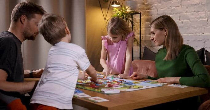 family with two children sitting by the table and playing board games at home