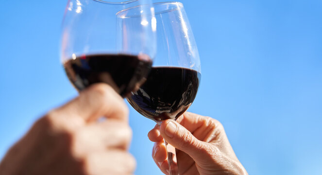 Celebration and enjoyment concept. Two hands toast with glass of  wine over blue sky with copy space 