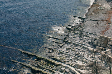 vue d'en haut sur la ligne diagonale qui sépare la mer d'une plage de roche grise en été - obrazy, fototapety, plakaty