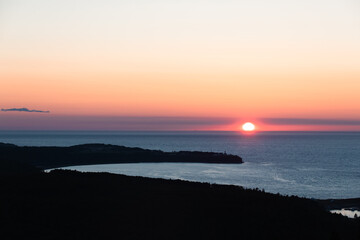 vue sur la mer lors d'un coucher de soleil avec les derniers rayons lumineux et des teintes de rose et orange dans le ciel