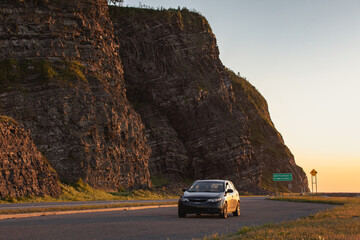 vue sur une voiture noire sur une route au bord d'une falaise lors d'un coucher de soleil en été - obrazy, fototapety, plakaty