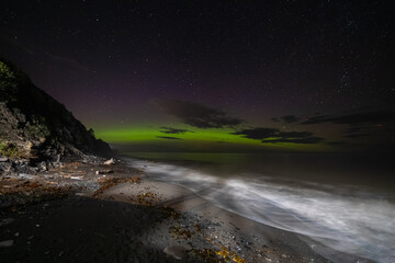 vue sur une plage la nuit avec les premières lueurs d'une aurore boréale verte dans le ciel