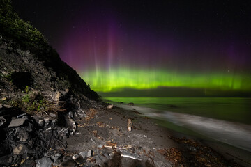 vue sur une plage la nuit avec la lumière d'une aurore boréale mauve et verte qui danse dans le...