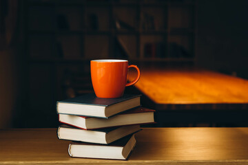 An orange cup on a stack of books on a dark library background. Book background. Education,...