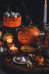 Homemade delicious chocolate cake with coloured orange cream and meringue ghosts, pumpkins for Halloween home party. Elegant beautiful table arrangement with candles, chandelier, Jack-o-Lantern