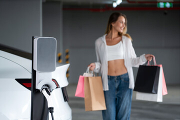 Young woman travel with EV electric car to shopping center parking lot charging in downtown city...